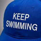 Close-up of white Keep Swimming embroidery on the blue baseball cap